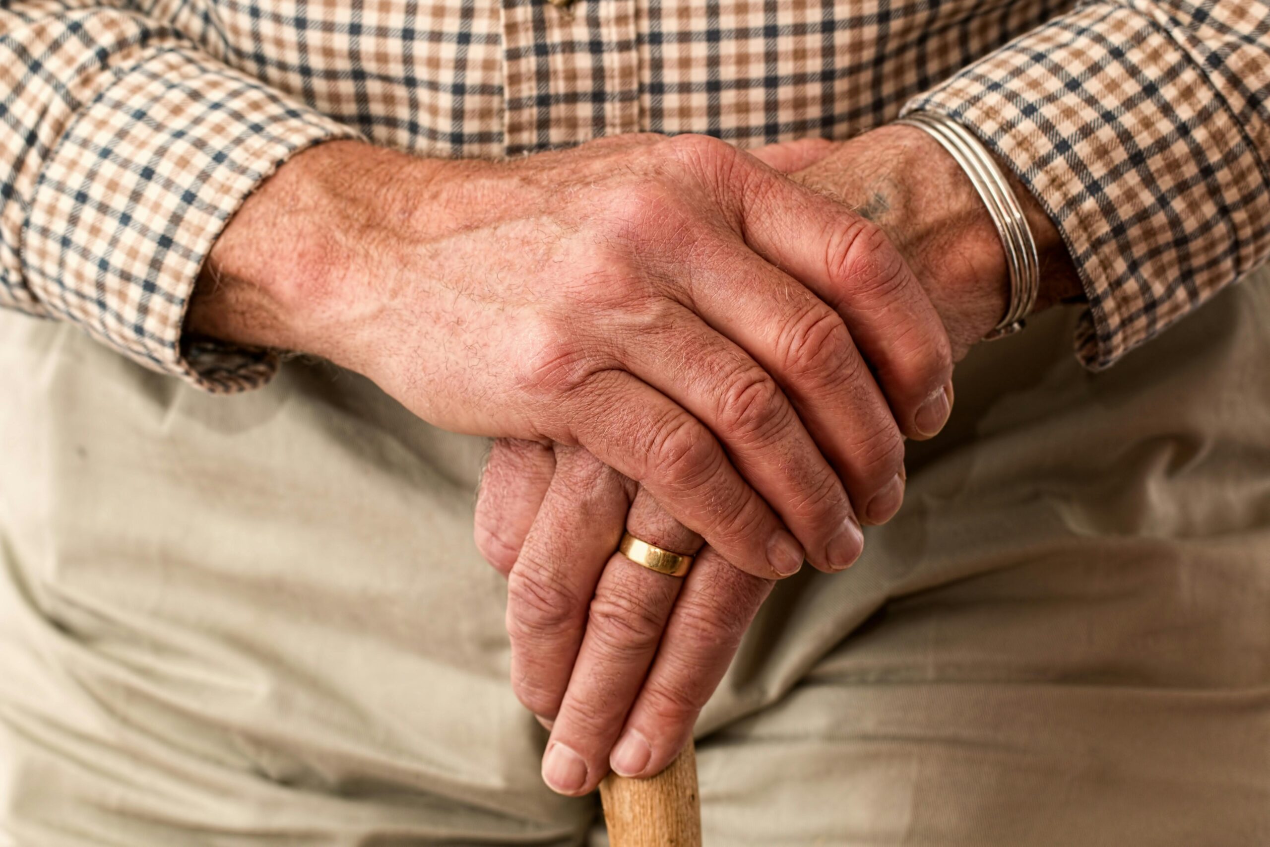 hands-walking-stick-elderly-old-person-33786 A detailed image of elderly hands clasping a wooden cane, symbolizing aging and support.