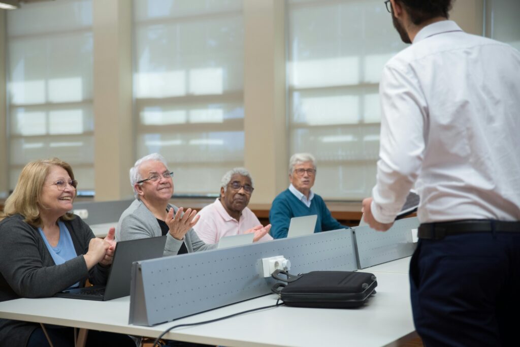 Senior adults attend a computer class, led by an instructor, in a classroom setting.